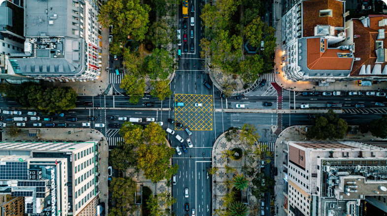 Numa vista aérea vemos um cruzamento de ruas de uma grande cidade com muito trânsito