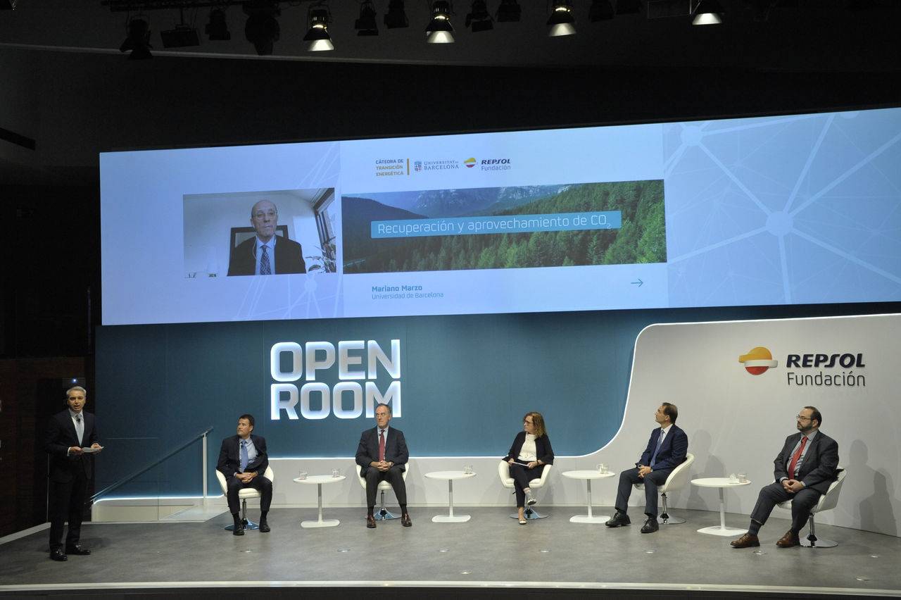 An auditorium stage decorated with the Open Room brand and several speakers seated waiting to speak.