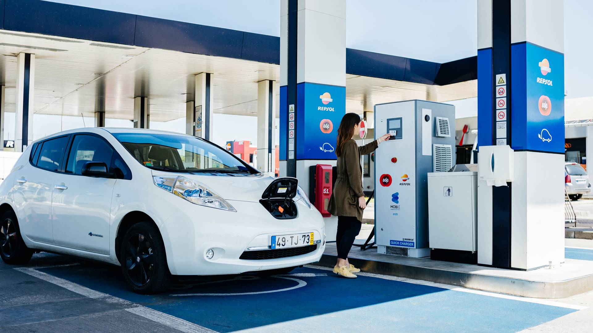 Mujer recarga su coche eléctrico en estación de servicio