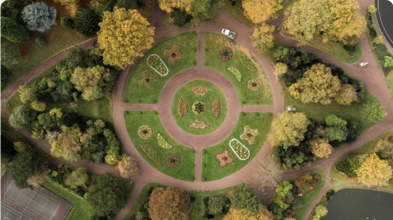 Vemos uma praça circular de um parque a partir do céu, jardins e copas das árvores